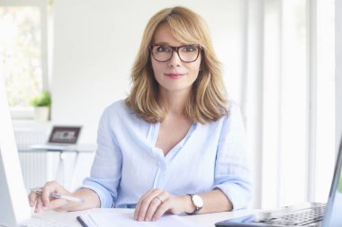 Güzel bir orta doz ofis masası oturma ve çalışma bilgisayar ve laptop süre biraz evrak işi yapıyor işkadını yaşlı. Çoklu görev.