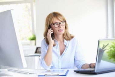 Dizüstü bilgisayarda çalışan office masasında otururken cep telefonu müvekkili ile konuşurken çekici olgun işkadını yakın çekim portresi.