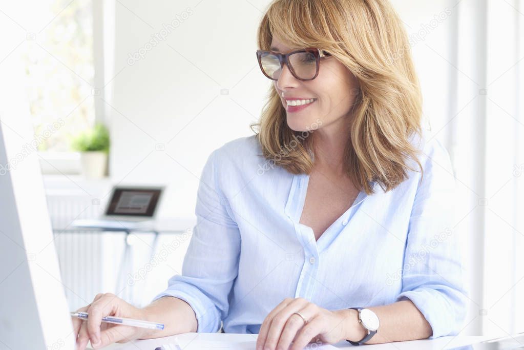Close-up sho of beautiful sales woman with toothy smile working on computer at modern office. 
