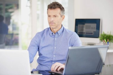 Ofiste iş istasyonunda çalışırken dizüstü kullanarak düşünme rahat bir iş adamı. Çoklu görev. 