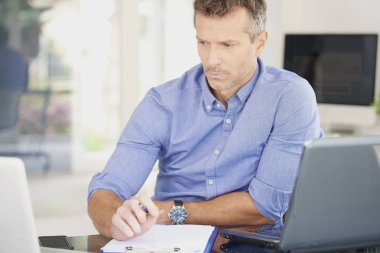 Düşünme işadamı ofis masasında otururken dizüstü ve dolgu formu üzerinde çalışan orta yaşlı. 