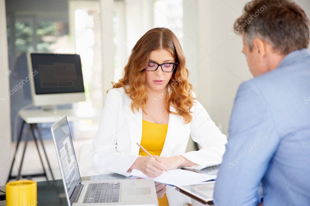 Confident businesswoman sitting at office desk and making notes while consulting with her client. 