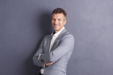 Gri duvara ayakta ve kameraya bakarak katlanmış silah ile kendine güvenen bir orta yaşlı işadamı yakın çekim portre vurdu. 