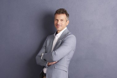 Kendine güvenen orta yaşlı işadamı ile portre çekim gri duvara ayakta ve kameraya seyir silah katlanmış.