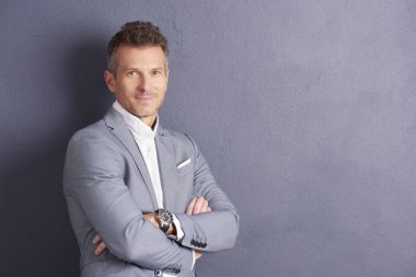 Kendine güvenen orta yaşlı işadamı ile portre çekim gri duvara ayakta ve kameraya seyir silah katlanmış.