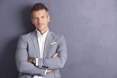 Kendine güvenen orta yaşlı işadamı ile portre çekim gri duvara ayakta ve kameraya seyir silah katlanmış.