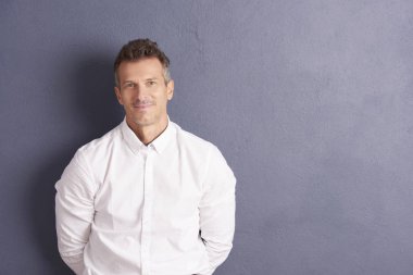 Casual adam kameraya bakarak ve gülümseyen gri duvara ayakta. 