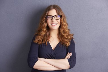 Katlanmış silah gri duvara poz ile mutlu genç kadın portresi. 