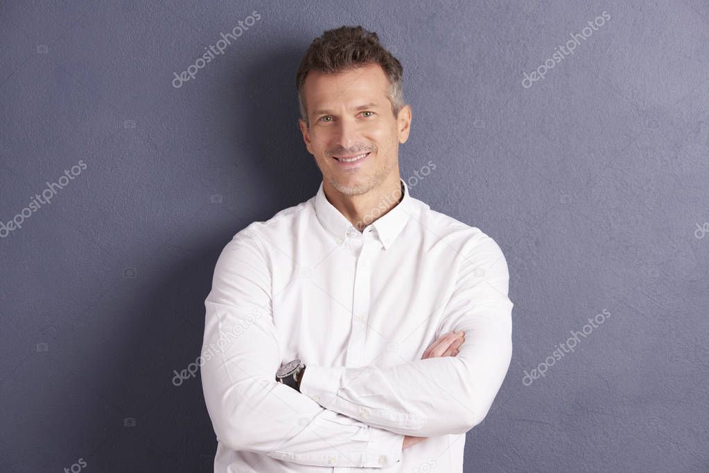 Portrait of middle aged businessman wearing shirt while standing with folded arms at grey background. 