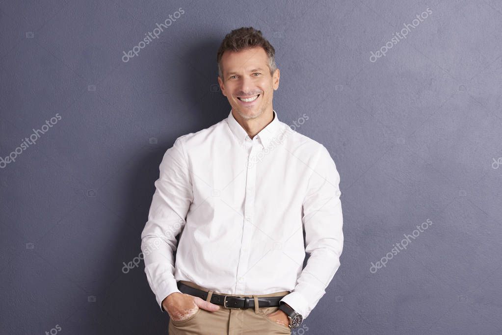 Casual man standing at grey wall while looking at camera and smiling. 