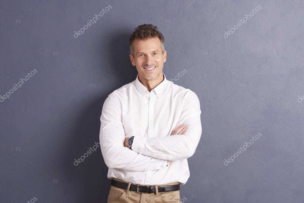 Portrait of middle aged businessman wearing shirt while standing with folded arms at grey background. 