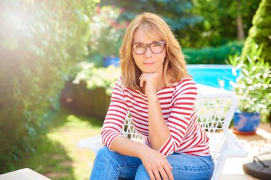 Bahçede oturan açık ve rahatlatıcı kendinden emin ve güzel orta yaşlı bir kadın portresi. 