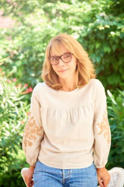 Açık ve size gülümseyen ayakta iken rahat kıyafetler giymiş güzel olgun kadın portresi.