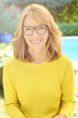 Güzel oturan orta yaşlı kadın gülümseyerek ve bahçede evde rahatlatıcı kırpılmış atış. 