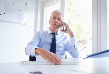 Ofis Masası oturma ve onun cep telefonu konuşurken üst düzey iş adamı. Gömlek ve kravat giyen yaşlı profesyonel adam. 