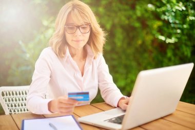 Çekici orta yaşlı kadın evden dizüstü bilgisayar ve e-bankacılık yaparken kredi kartı kullanarak yüksek açı çekim. 