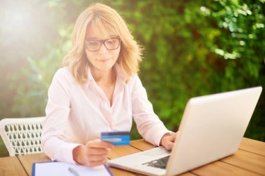 Çekici orta yaşlı kadın evden dizüstü bilgisayar ve e-bankacılık yaparken kredi kartı kullanarak yüksek açı çekim. 