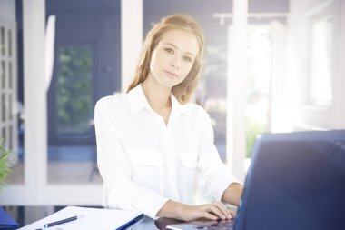 Laptopunu kullanıyor ve ofis masa başında otururken güzel genç iş kadını.