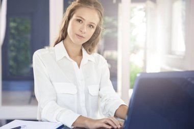 Laptopunu kullanıyor ve ofis masa başında otururken güzel genç iş kadını.