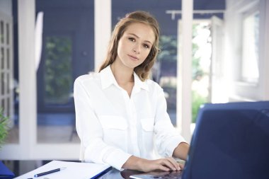 Laptopunu kullanıyor ve ofis masa başında otururken güzel genç iş kadını.