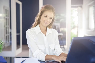 Laptopunu kullanıyor ve ofis masa başında otururken güzel genç iş kadını.