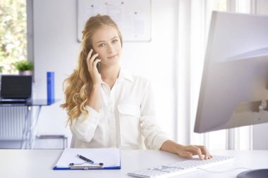 Biri ile onu cep telefonundan konuşuyor ve ofiste otururken bilgisayarını kullanarak güzel genç mali asistanı işkadını portresi.