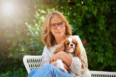 Shot of happy middle aged woman sitting outdoor with her cute dog. clipart