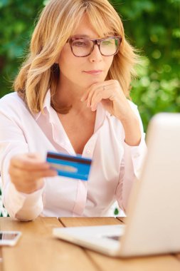 Açık havada oturma ve online alışveriş yaparken onun kredi kartı ve dizüstü kullanarak orta yaşlı kadın. 