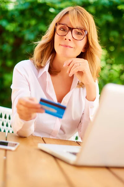 中年妇女坐在户外 并使用她的信用卡和笔记本电脑 而网上购物 — 图库照片