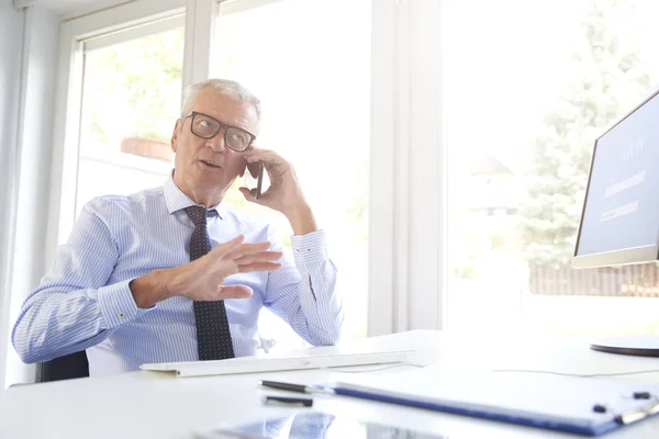 Shot of a senior financial director businessman using cell phone while talking with somebody in the office.