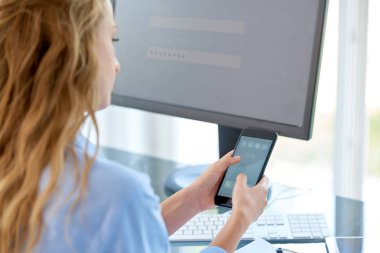 Genç işkadını onun cep telefonu ve bilgisayar önünde ofis masasında otururken mesajlaşma metin kullanarak kadeh görünümü arka ve online banka için şarkı. 