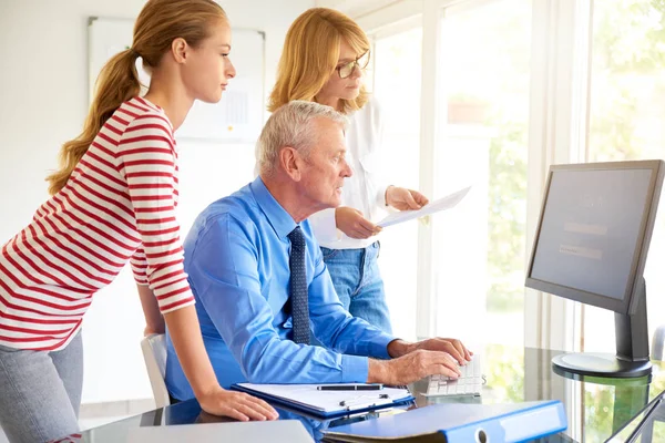 Shot of senior financial director businessman sitting in front of computer and talking with his colleagues. Teamwork in the office.