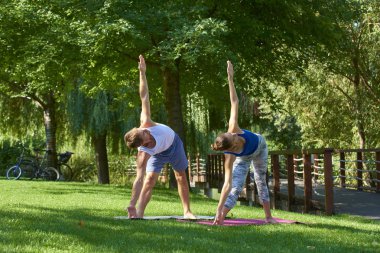 Genç adam kadın eğitim yoga birlikte parkta bir kadeh tam uzunlukta. Yoga açık yaparken çift.