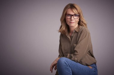 Stüdyo ışık gri arka plan önünde oturan çekici orta yaşlı kadın portresi. 