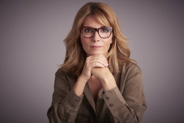 Stüdyo gri arka plan otururken kameraya bakarak emin Olgun kadın portresi.