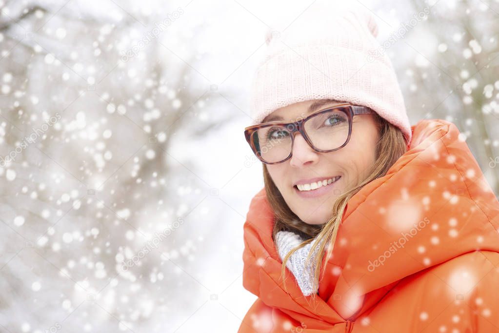 Close-up portrait of middle aged woman wearing hat while standing outdoor and enjoy winter weather in the snwofall.