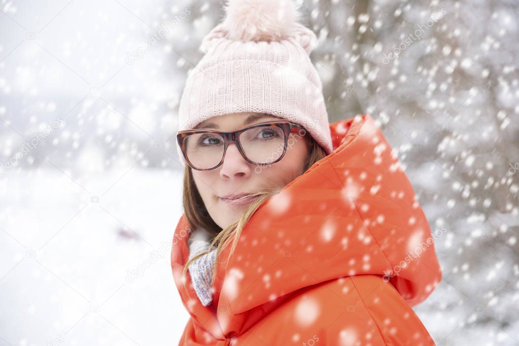 Close-up portrait of middle aged woman wearing hat while standing outdoor and enjoy winter weather in the snwofall.