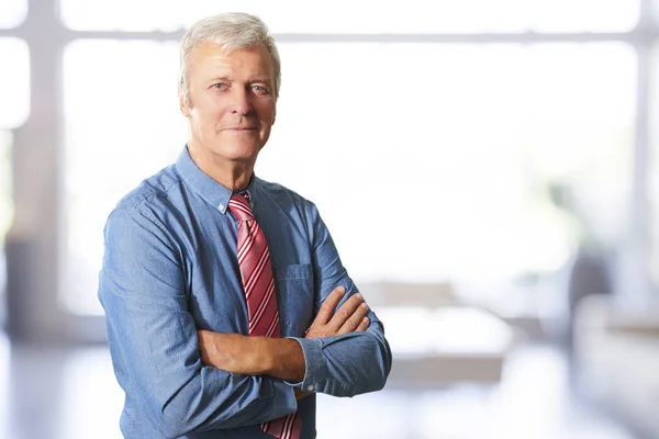 Portrait of an executive senior businessman standing at office with arms crossed.