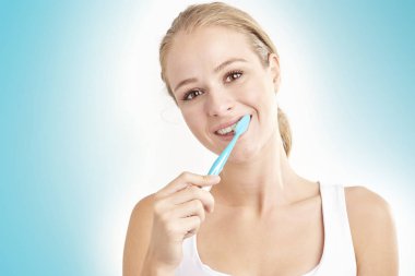 Kameraya bakarak ve gülümseyen dişlerini fırçalama güzel genç kadının Studio vurdu. Açık mavi renkli izole.