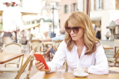 Onun cep telefonu ve kafede otururken mesajlaşma metin kullanarak gülümseyen çekici kadın portresi.