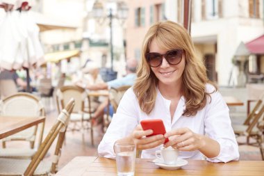 Onun cep telefonu ve kafede otururken mesajlaşma metin kullanarak gülümseyen çekici kadın portresi.