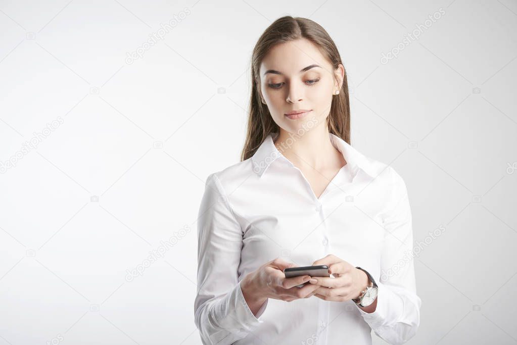 Beautiful young businesswoman wearing white shirt and text messaging while standing against at isolated white background.