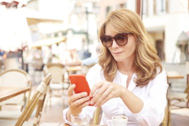 Onun cep telefonu ve kafede otururken mesajlaşma metin kullanarak gülümseyen çekici kadın portresi.