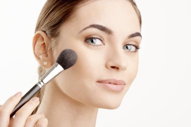 Yakın çekim fırça onun elinde tutan ve makyaj uygulayarak genç bir kadın. Beyaz arka plan üzerinde izole.