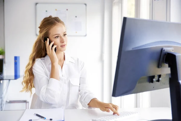 美丽的年轻女商人坐在办公桌前的电脑前 在办公室工作时打电话 — 图库照片