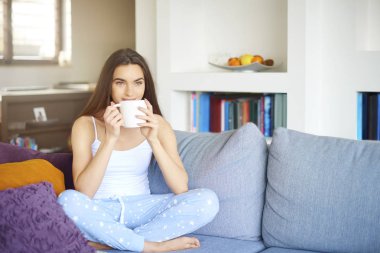 Atış pijama giymiş ve erken sabah koltukta dinlenirken çay içme genç güzel kadın.