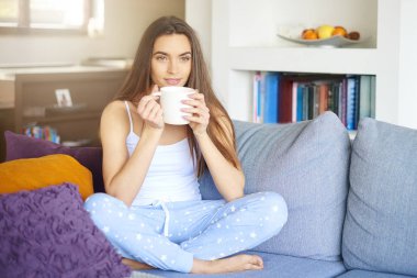Atış pijama giymiş ve erken sabah koltukta dinlenirken çay içme genç güzel kadın.