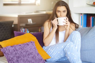 Atış pijama giymiş ve erken sabah koltukta dinlenirken çay içme genç güzel kadın.