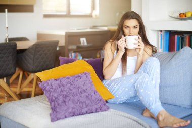 Atış pijama giymiş ve erken sabah koltukta dinlenirken çay içme genç güzel kadın.