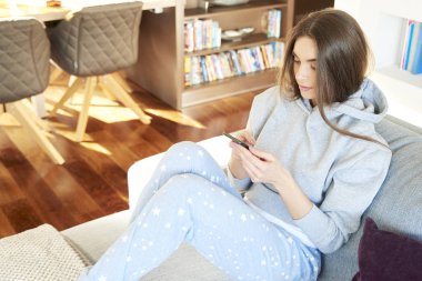 Yüksek açı çekim hoodie ve metin mesajlaşma koltukta evde dinlenirken giyen güzel genç kadın. 